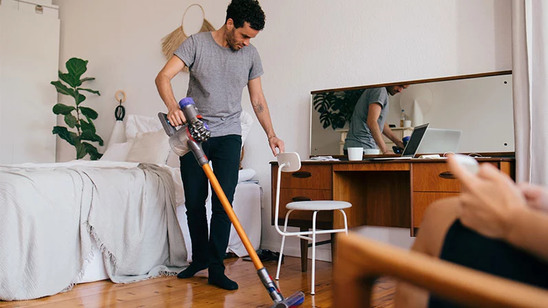 A man vacuuming her bedroom in the daytime.